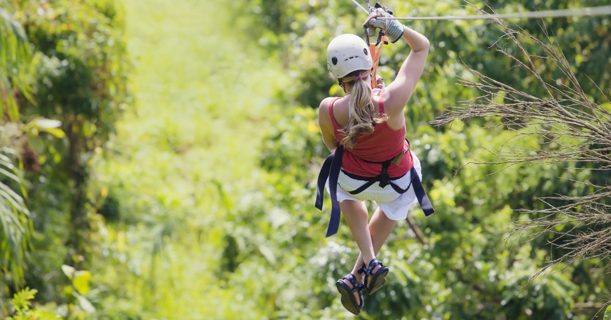 a woman ziplining over the tops of trees