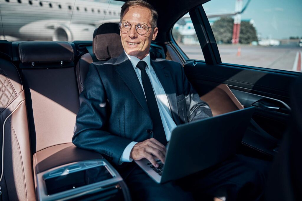 cheerful-businessman-with-laptop-in-car-at-airport